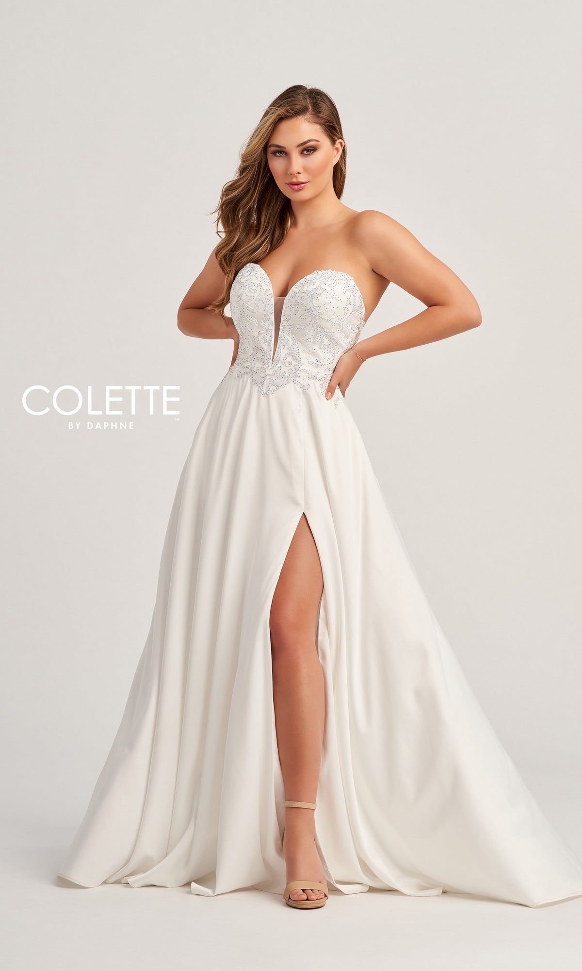 A woman wears the Colette Strapless Long Designer Prom Dress CL5142, featuring a fitted embellished bodice, high skirt slit, and elegant white strapless design—ideal for anyone seeking a chic prom gown.